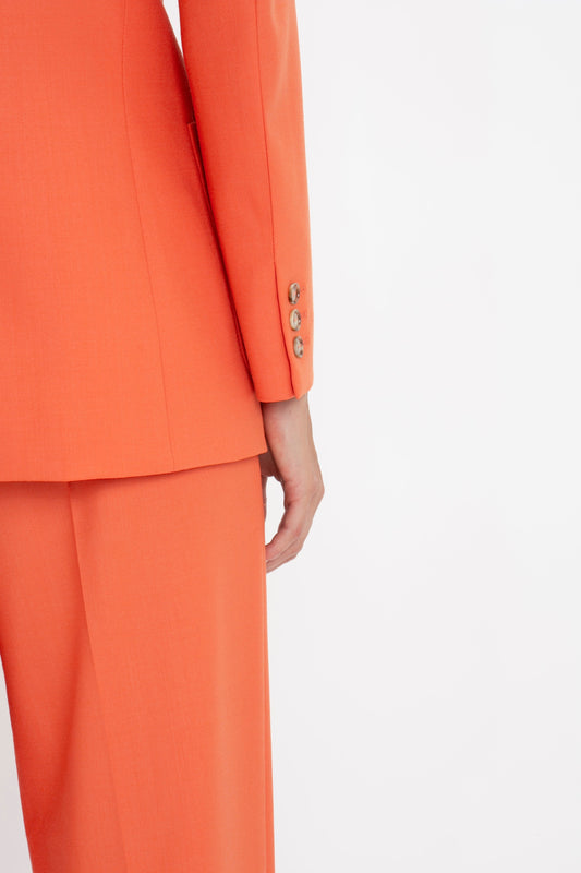 Close-up of a woman in an elegant Victoria Beckham patch pocket jacket in papaya with detailed button cuffs, standing with her hand at her side.