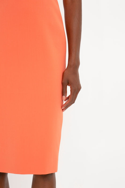 Close-up of a woman in a Victoria Beckham Fitted T-shirt Dress In Papaya, focusing on her side as she gently pinches the fabric near her thigh.
