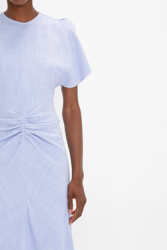 A person in a Victoria Beckham light blue midi dress with short sleeves and a gathered fabric design at the waist, cropped to show from the neck down.