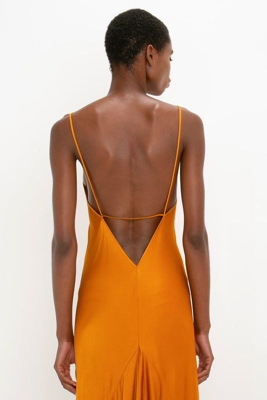 Woman from behind wearing an elegant, mustard yellow Victoria Beckham Floor-Length Cami Dress in Ginger with a plunging backline and thin straps.