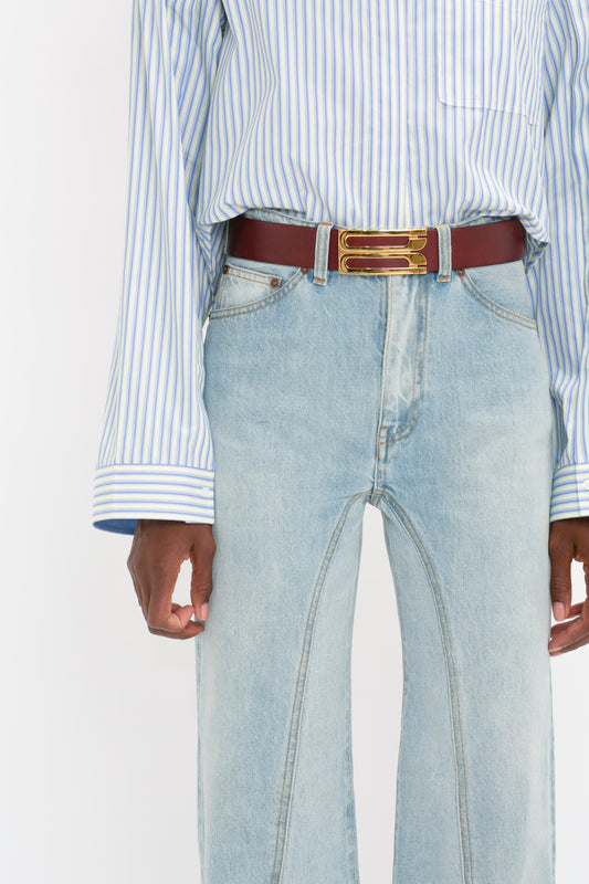 Close-up of a person wearing a blue striped cropped shirt with button detail and Victoria Beckham's Bianca Jean in Light Blue Denim. Only the torso and hands are visible.
