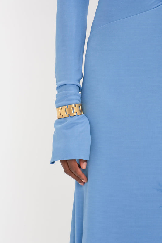 Close-up view of a woman's side, wearing a Victoria Beckham High Neck Asymmetric Draped Dress In Oxford Blue with a stylish gold bracelet. Only her arm and part of her torso are visible.