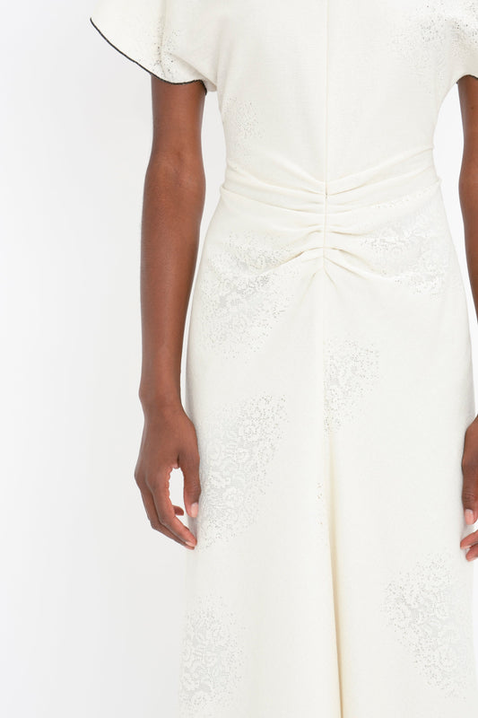 Close-up of a woman wearing an elegant white Victoria Beckham midi dress with lace details and a gathered waist, focusing on the torso and arm.