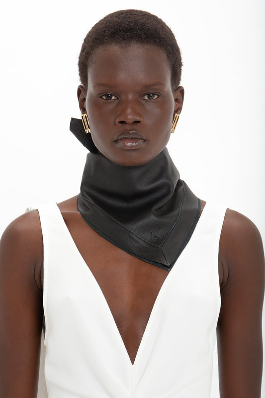 A woman with short hair wearing a white v-neck top and a Victoria Beckham black leather foulard, looking directly at the camera.