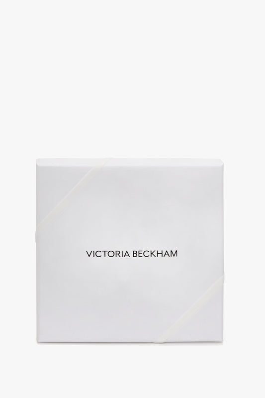 White gift box with a glossy finish, featuring the name "Victoria Beckham" in black text, secured with a subtle ribbon and containing Exclusive Over The Knee Socks In Black.