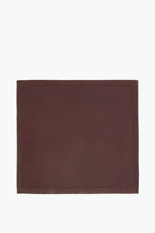 A brown supple Foulard In Bordeaux leather placemat with a simple stitched border, displayed on a plain background by Victoria Beckham.