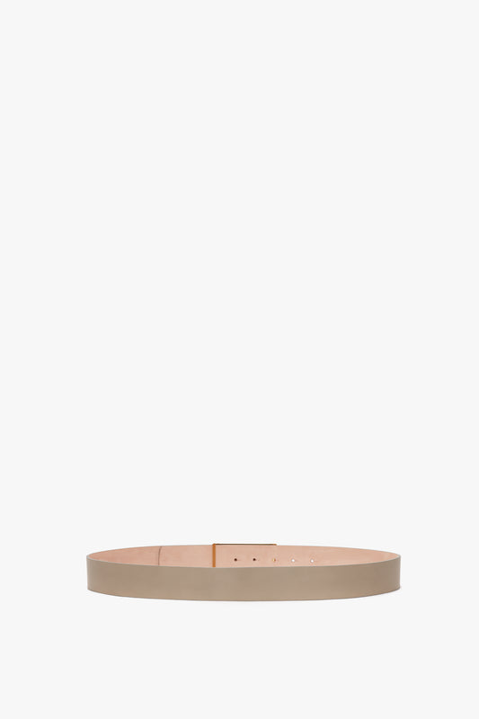 A thin, beige Exclusive Jumbo Frame Belt in calf leather laid out straight on a solid gray background by Victoria Beckham.