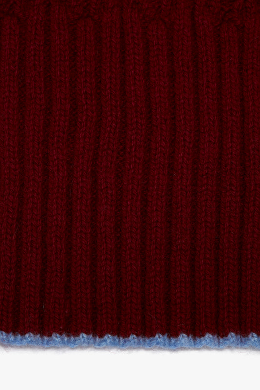 Close-up of a red knitted luxury scarf with distinct vertical ribbing and a thin blue thread at the bottom edge featuring a Victoria Beckham logo.
