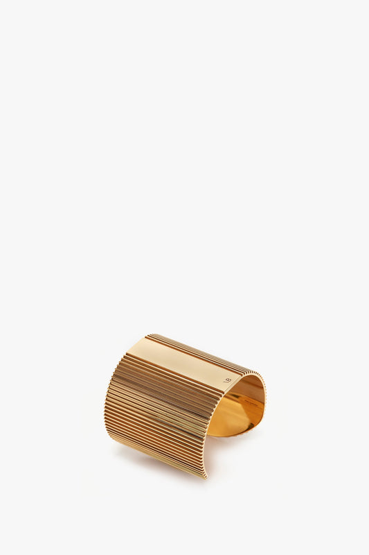 Victoria Beckham's exclusive perfume cuff in gold, with multiple horizontal lines, displayed on a white background.