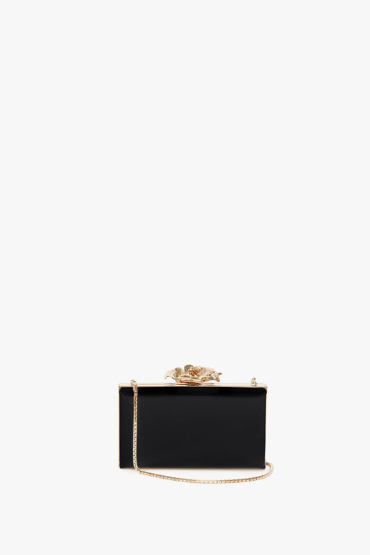 Black Frame Flower Minaudiere clutch purse by Victoria Beckham, with a floral clasp and brass frame, isolated on a white background.