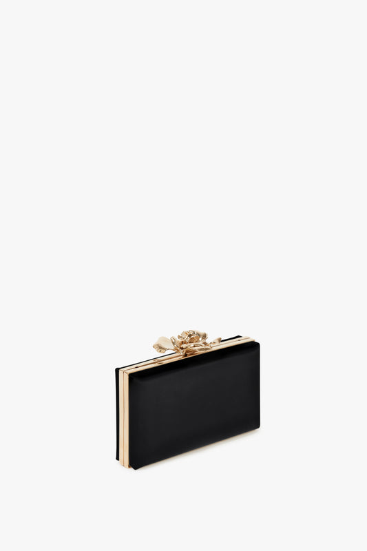 Victoria Beckham's Frame Flower Minaudiere in Black with gold trim and a floral clasp on a white background.