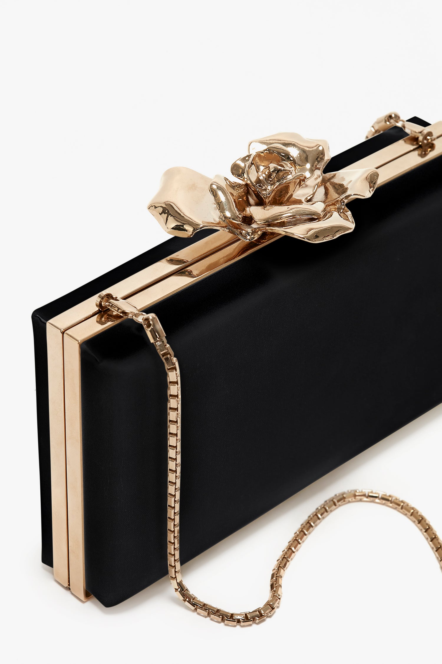 Black rectangular clutch with gold trim and a large gold floral clasp, accompanied by a thin gold chain strap, set against a white background. This hand-crafted Frame Flower Minaudiere from Victoria Beckham features a brass frame.