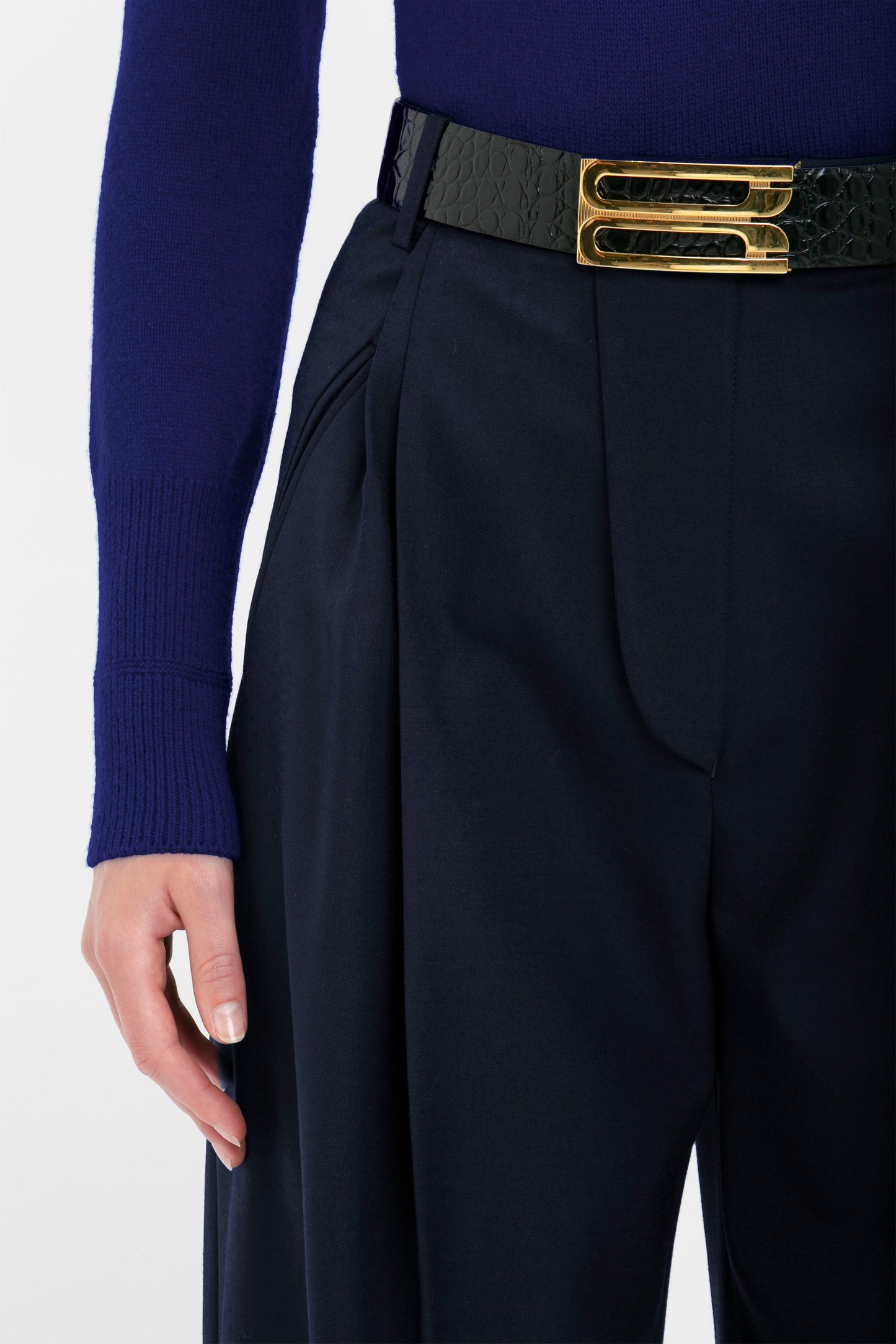 A person wearing a Polo Neck Jumper In Navy by Victoria Beckham and high-waisted black pants with a textured black belt featuring a gold clasp.