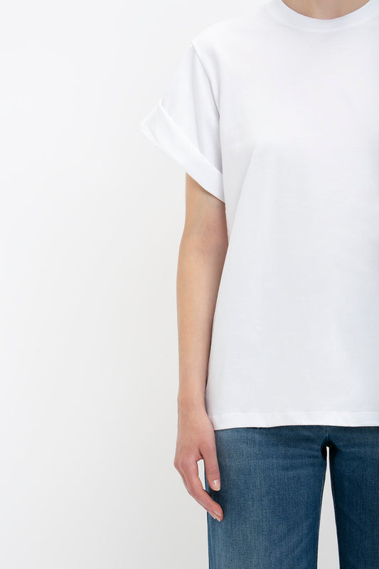 A person wearing an oversized Victoria Beckham T-shirt and blue jeans, photographed from neck to mid-thigh against a white background.