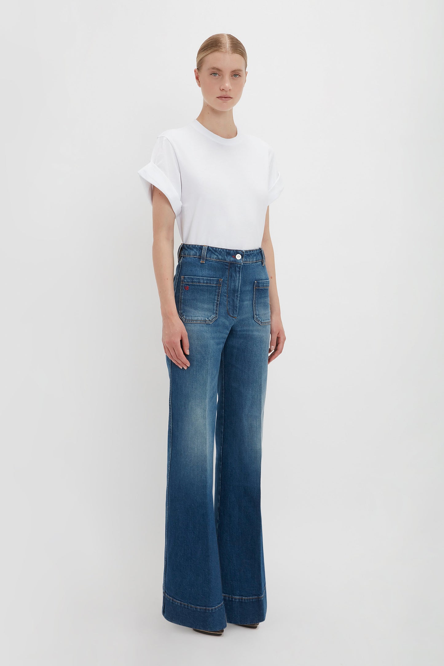 A woman in an oversized Victoria Beckham T-shirt and blue Alina jeans in Dark Vintage Wash stands against a white background, looking directly at the camera.
