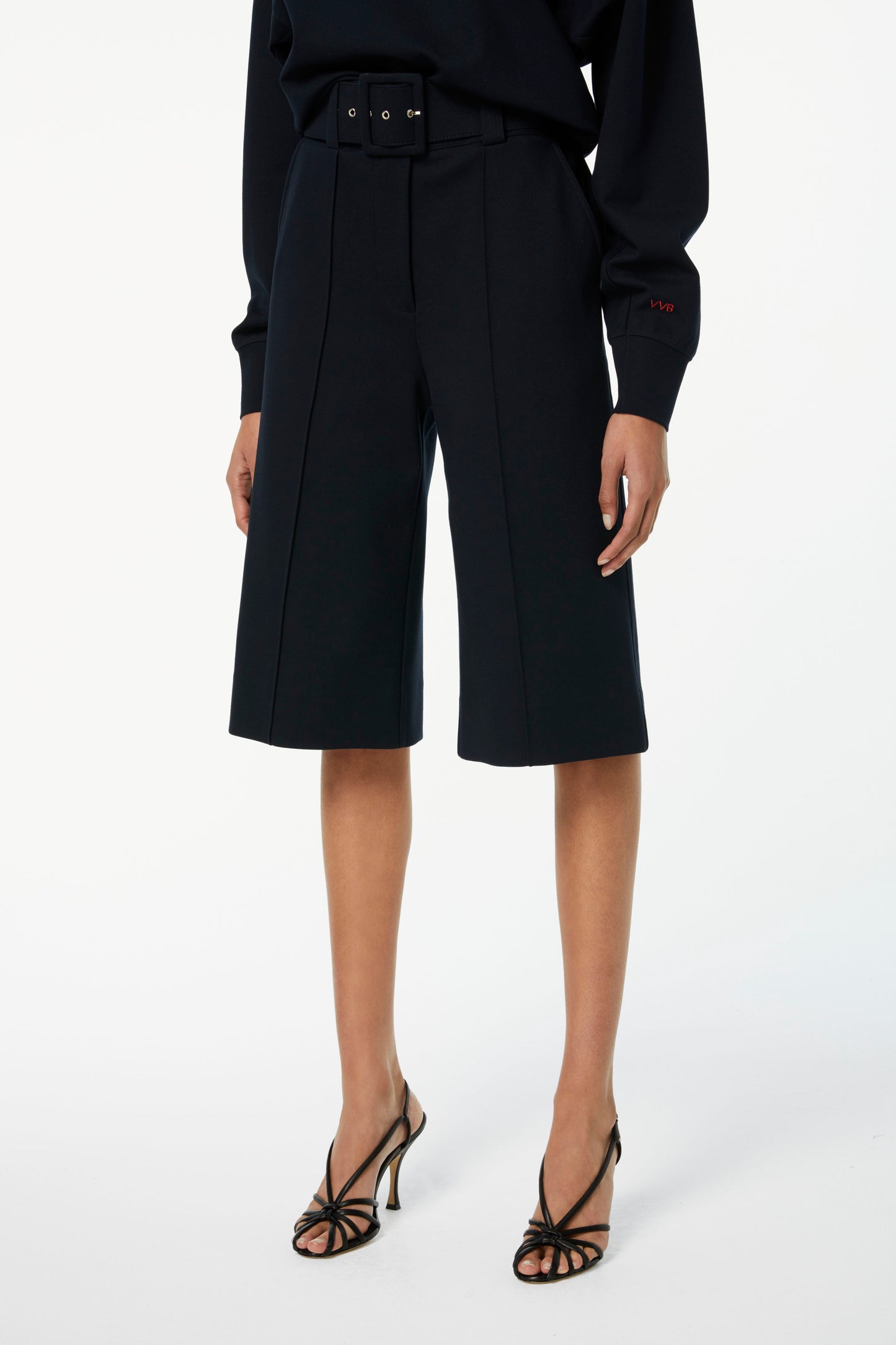 A person wearing a black ponte jersey long-sleeve top, Victoria Beckham Belted Jersey Culottes in Dark Navy, and black high-heeled sandals.