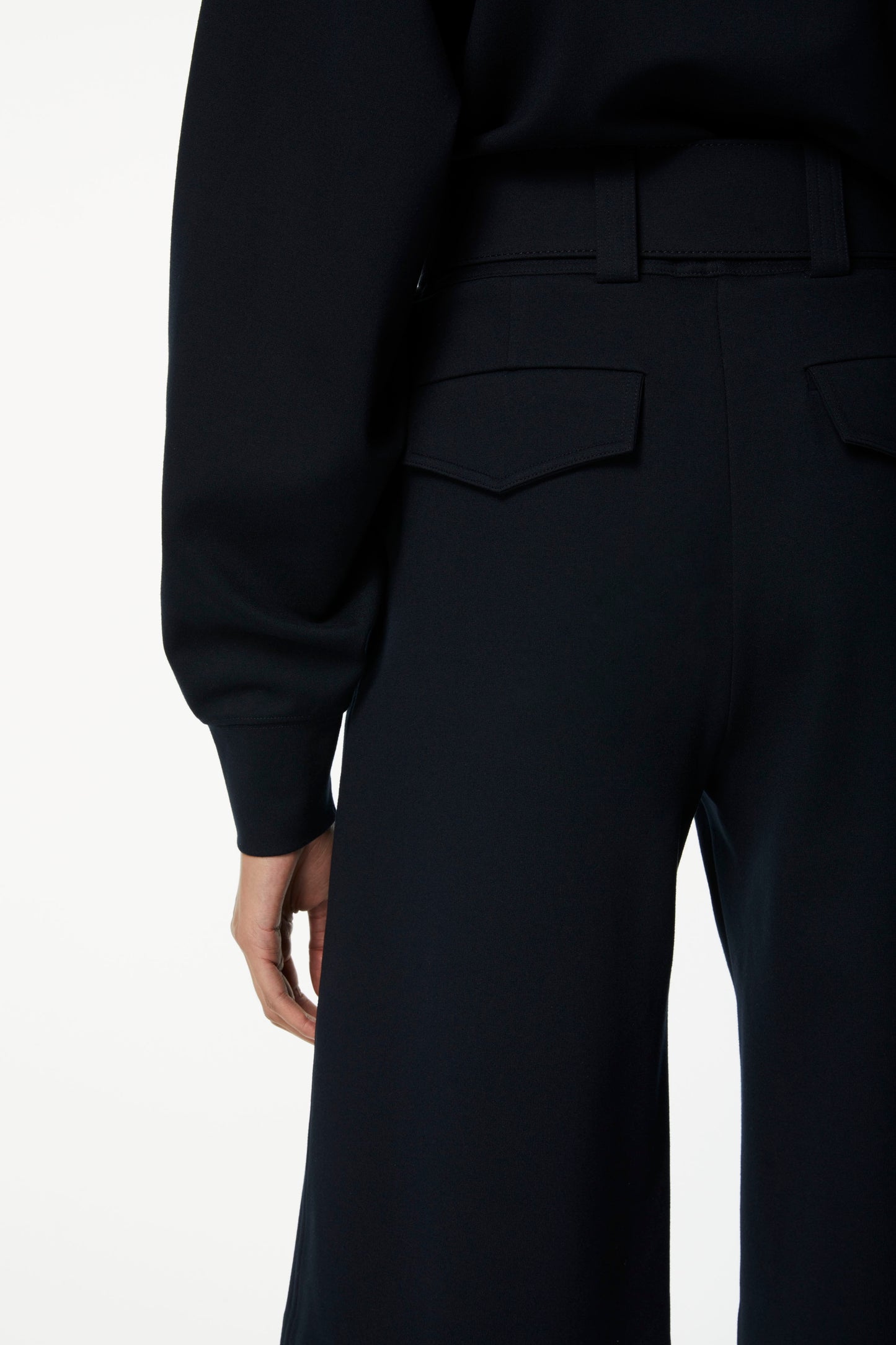 Close-up view of a person wearing Victoria Beckham Belted Jersey Culottes in Dark Navy with two back pockets, paired with a black long-sleeved top. The ponte jersey material ensures a flattering fit.