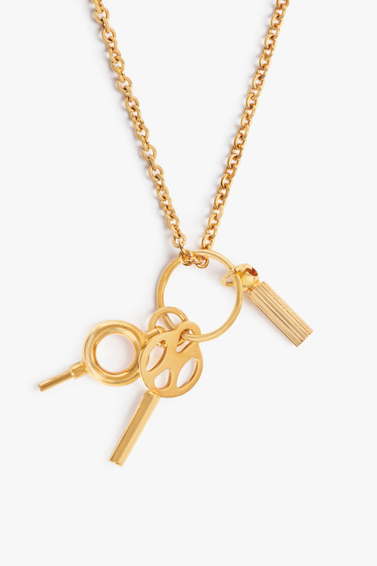 Victoria Beckham Key Charm Necklace in Gold with a chunky chain featuring a key, a round magnifying glass, and a tasseled charm, isolated on a white background.