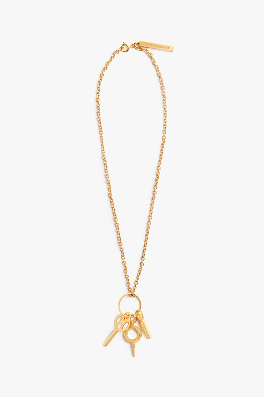 Victoria Beckham's Key Charm Necklace in Gold, with a clasp and attached charms including keys and a circular design, isolated on a white background.
