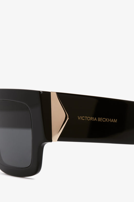 Close-up of black Victoria Beckham V Plaque Frame Sunglasses with a gold triangular accent on the temple.
