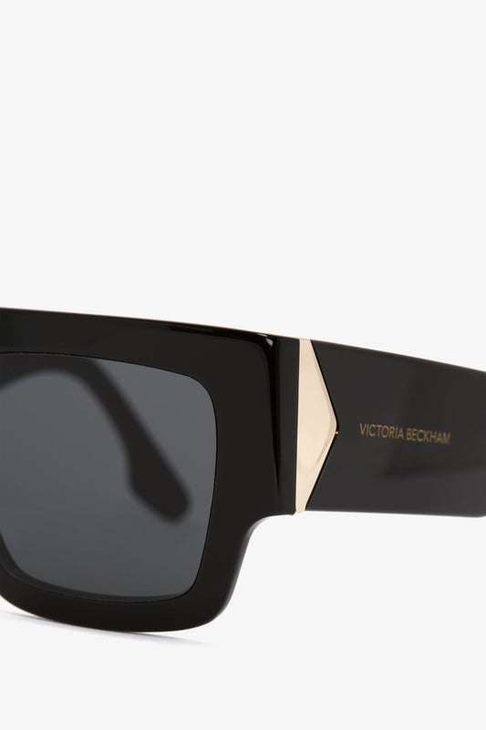 Close-up of a black rectangular Victoria Beckham V Plaque Frame Sunglasses with a gold accent on the high-shine acetate frame, isolated on a white background.