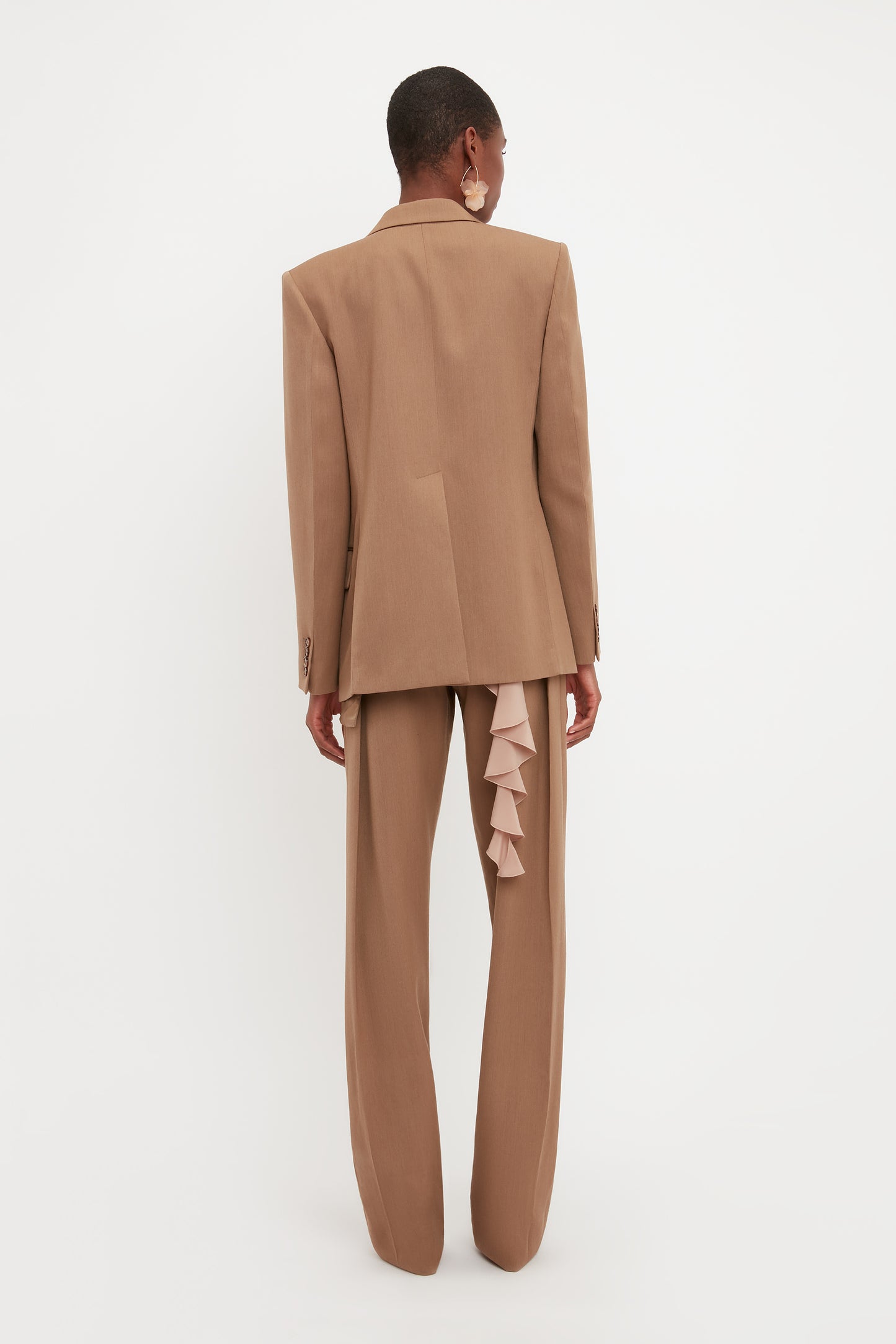 A person is wearing the Victoria Beckham Asymmetric Double Layer Jacket In Fawn, standing against a white background, facing away from the camera.