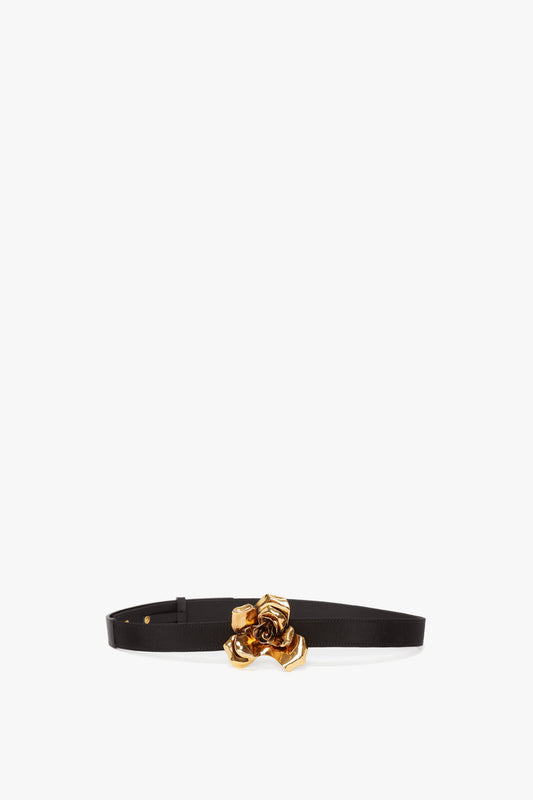 An Exclusive Flower Belt In Black And Gold by Victoria Beckham, with a gold-plated sculptural floral buckle, displayed against a plain white background.