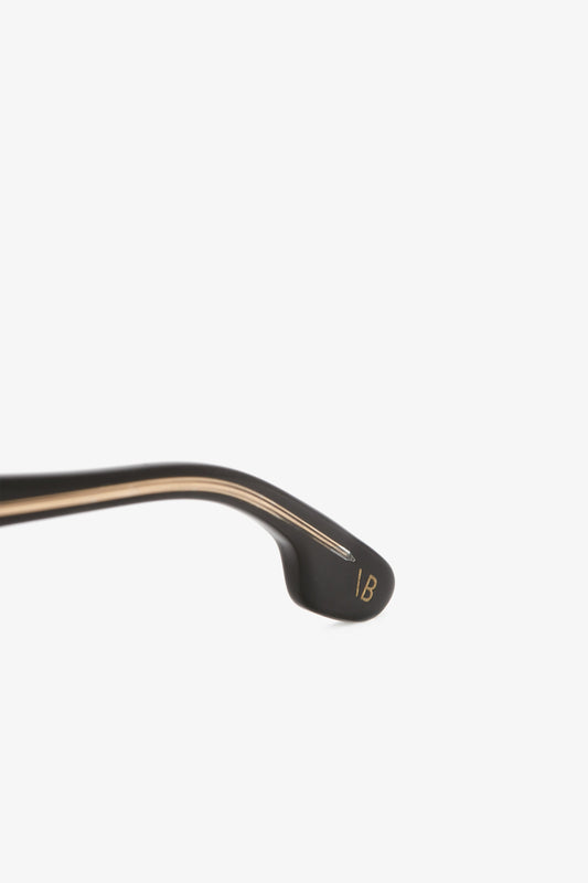 Close-up of a black and gold Victoria Beckham crowbar with the initials "ib" engraved on the curved end, against a plain white background.