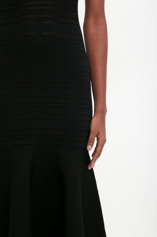 Close-up of a woman in a Victoria Beckham black knit top and fit-and-flare skirt, focusing on her side and arm.