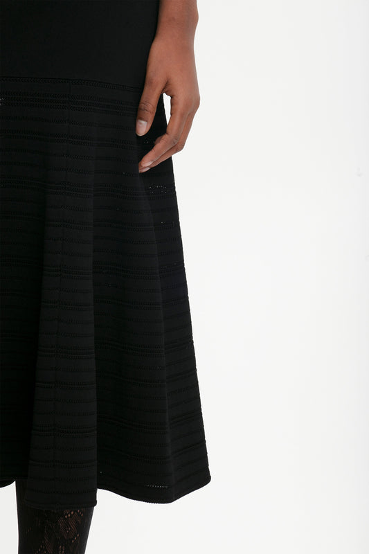 A person wearing the Victoria Beckham Fit And Flare Midi Skirt In Black with contrasting stitching and a hand resting on the side. The background is plain white.