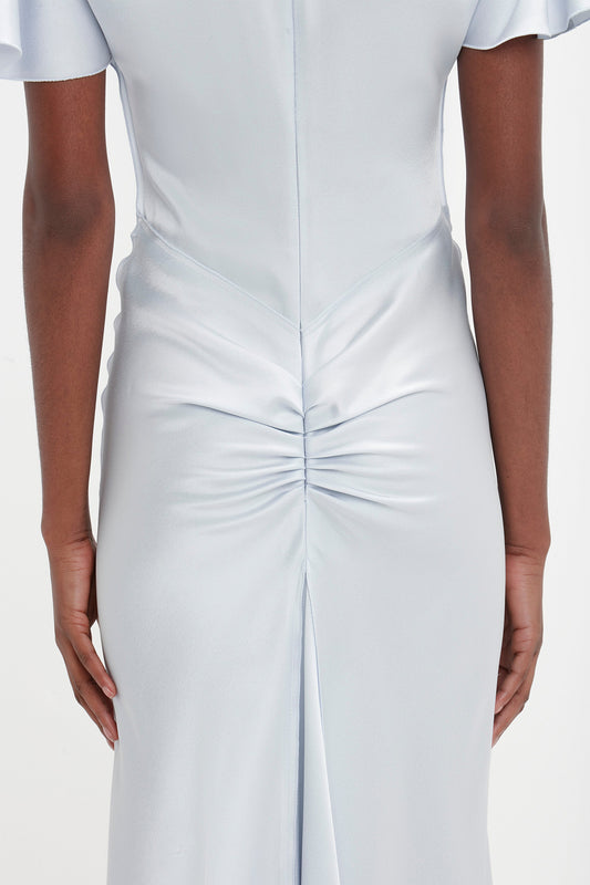Close-up of a person wearing an elegant Gathered Sleeve Midi Dress In Ice by Victoria Beckham, showing the back details including a seam running down the center, slight ruching at the base of the spine, and a subtle godet insert.