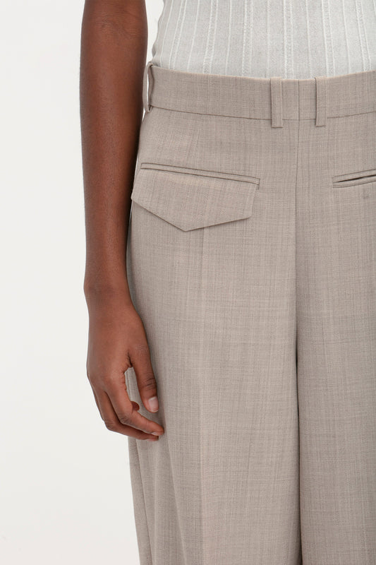 A person is wearing the Reverse Front Trouser In Sesame by Victoria Beckham with a side pocket flap and a light-colored, sleeveless, ribbed top, presenting a contemporary silhouette.