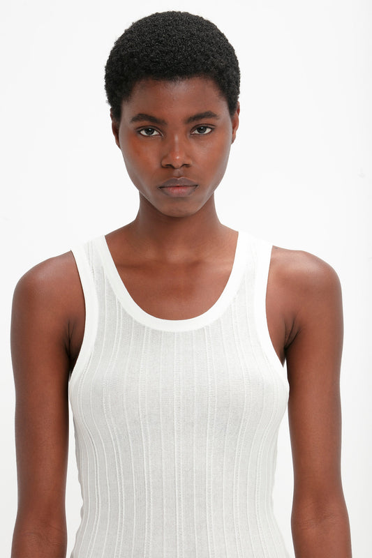 Person with short curly hair wearing a Fine Knit Vertical Stripe Tank In White by Victoria Beckham, looking directly at the camera against a plain, light background.