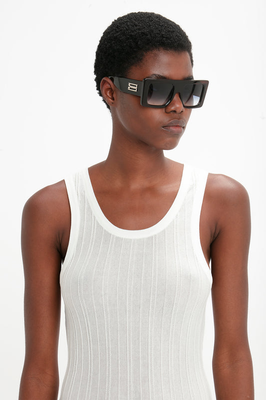 A person wearing sleek and modern, Victoria Beckham Oversized Frame Sunglasses In Black and a white sleeveless top stands against a plain white background.
