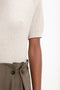 Close-up of a person wearing the Victoria Beckham Short Sleeve Top In Nougat and high-waisted olive trousers with large buttons and pleats. The image only shows part of the person's upper body.