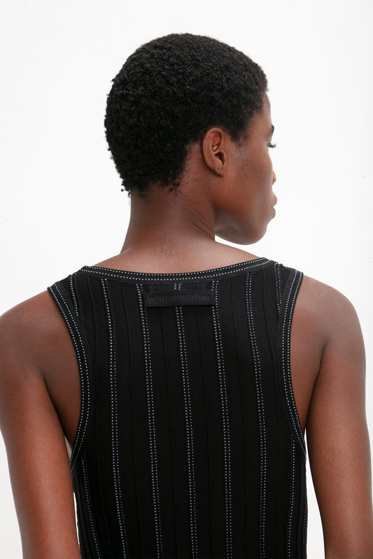 Person with short curly hair wearing a sleeveless black Fine Knit Vertical Stripe Tank In Black-Blue by Victoria Beckham, photographed from behind.