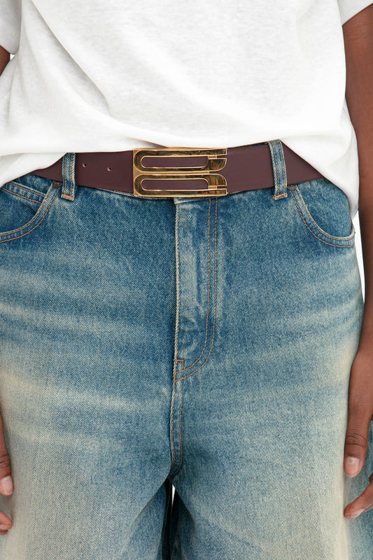 Person wearing Victoria Beckham Oversized Bermuda Short In Antique Indigo Wash with a brown belt featuring a large metal buckle, and a white t-shirt partially tucked in.