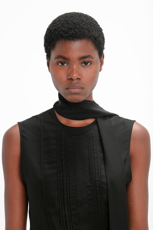 Person with short curly hair wearing a Victoria Beckham Sleeveless Tie Neck Top In Black, complemented by a matching scarf wrapped around the neck, looking directly at the camera.