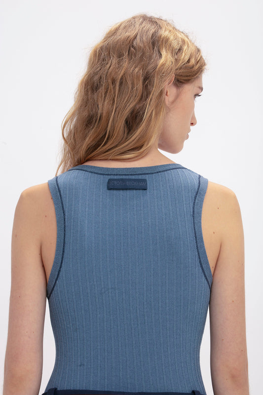 A person with wavy, light brown hair is seen from the back, wearing a sleeveless, ribbed Victoria Beckham Fine Knit Micro Stripe Tank In Heritage Blue.