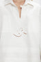 A person is wearing an Oversized Embroidered Tunic In Antique White by Victoria Beckham, featuring an embroidered design with geometric shapes and a swirl in the center. The garment has a V-shaped neckline with a small button closure at the top, reminiscent of Victoria's runway picks.