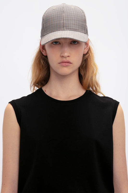 Young woman in a black sleeveless top wearing a Victoria Beckham Logo Cap In Dogtooth Check, looking directly at the camera.