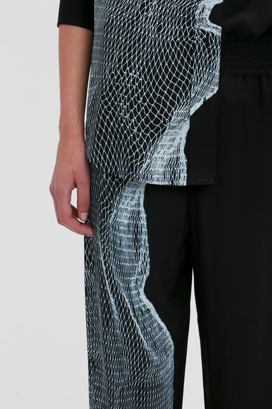 Close-up of a person wearing a black outfit with twisted net print on the jacket and wide leg Pyjama Trouser In Black-White Contorted Net by Victoria Beckham, with part of their left arm visible.