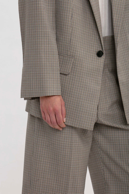 Close-up of a person wearing an oversized gray plaid suit jacket and matching trousers, with their hand partially visible by their side. The Peak Lapel Jacket In Multi by Victoria Beckham enhances the oversized silhouette, adding a touch of modern elegance.