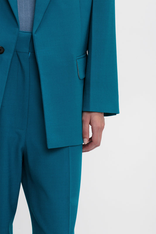 Person wearing a teal Peak Lapel Jacket In Petroleum and a blue top, with their right arm hanging straight beside their body. The oversized silhouette highlights the suit's detailed pocket and sleeve design, reminiscent of the Victoria Beckham brand.