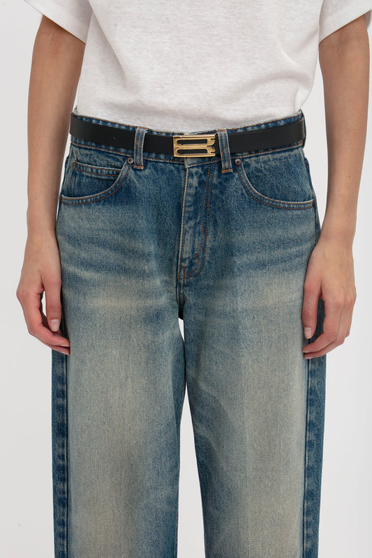 Close-up of a person wearing blue jeans with a Victoria Beckham Exclusive Frame Belt In Midnight Navy Leather, focusing on the waist area against a white background.