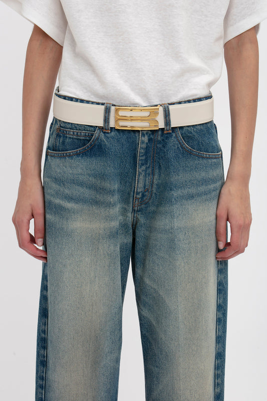Person wearing blue denim jeans, a white top, and a contemporary Victoria Beckham Jumbo Frame Belt In Latte Leather featuring a rectangular gold buckle.