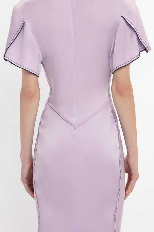 Back view of a person wearing the Gathered V-Neck Midi Dress In Petunia by Victoria Beckham, with short sleeves, waist-defining pleat, and visible seam details.