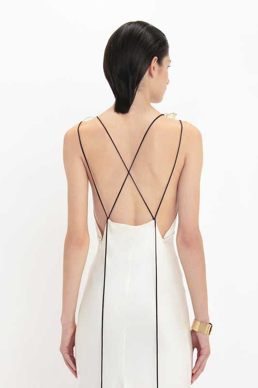 Person with short dark hair wearing a Victoria Beckham Gathered Shoulder Floor-Length Cami Gown In Ivory with thin black straps crossing at the back, viewed from behind.