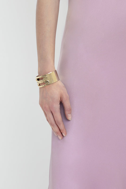 Close-up of a woman's arm wearing a gold cuff bracelet, hand resting against a deep V neckline of a Victoria Beckham Low Back Cami Floor-Length Dress In Rosa.