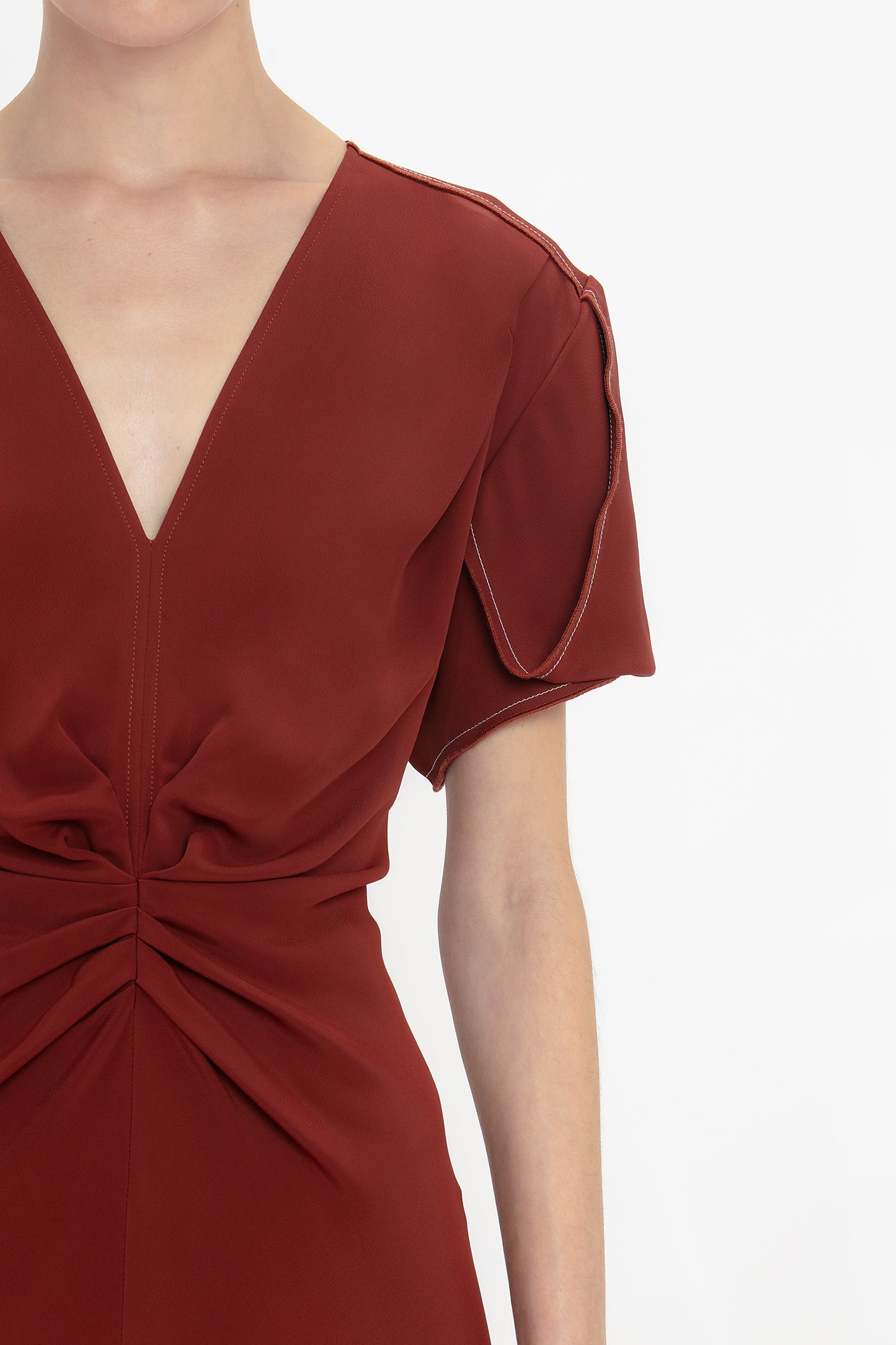 Close-up of a person wearing the Gathered V-Neck Midi Dress In Russet by Victoria Beckham. The figure-flattering stretch fabric showcases a waist-defining pleat detail.